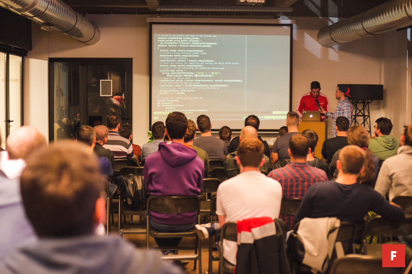 Many people watching a projector while another person is giving a presentation